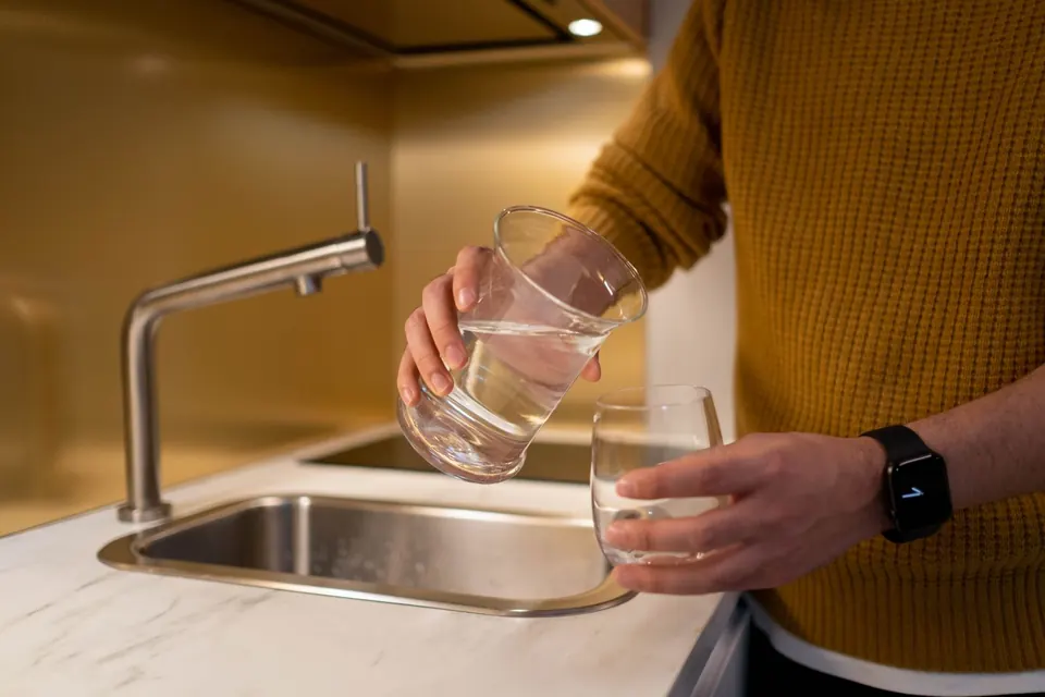Person pouring water from a pitcher into a glass in a contemporary kitchen setting.