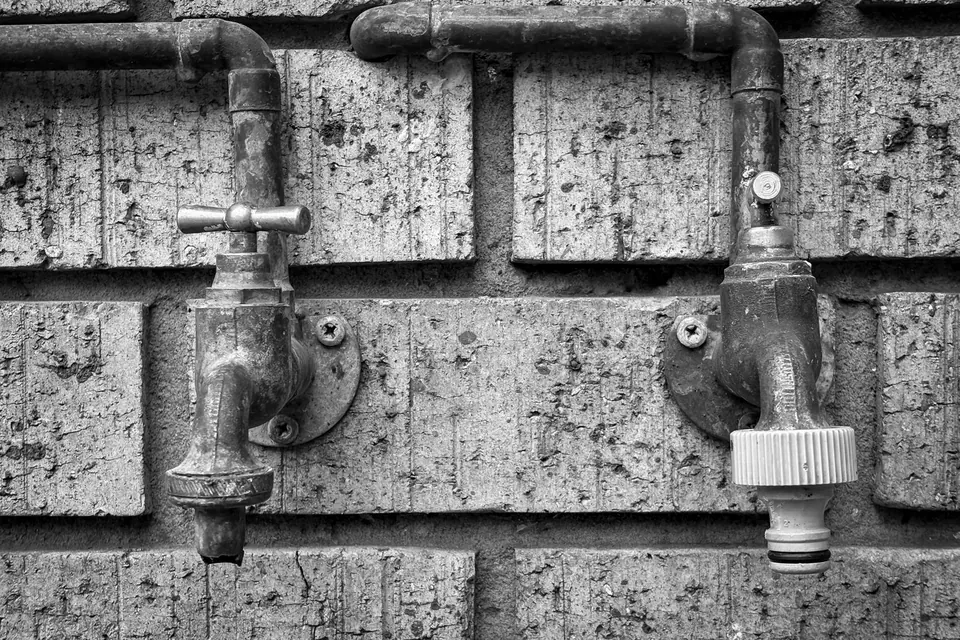 Close-up of vintage outdoor plumbing taps on a brick wall, black and white.